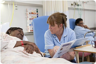 Female patient lying in a hospital bed talking to a nurse